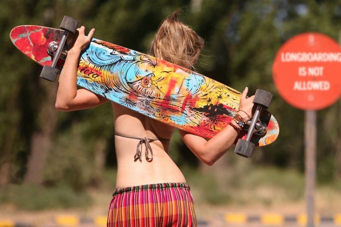 Woman carrying a longboard with a sign in the background