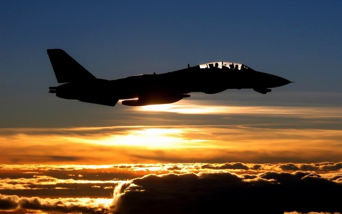 Silhouette of F-14 Tomcat fighter jet flying at sunset