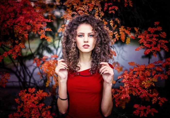 Woman in red dress with curly hair and autumn leaves