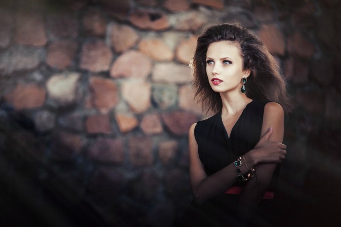 Woman with long hair and jewelry in front of stone wall