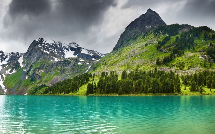 Turquoise lake with snow-capped mountains and green forest