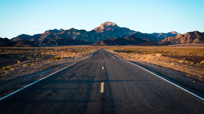Desert highway leading to mountains at sunrise