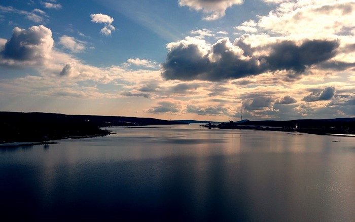Water body with industrial structures and clouds at sunset
