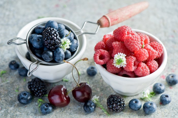 Bowls of fresh berries and cherries with small white flowers