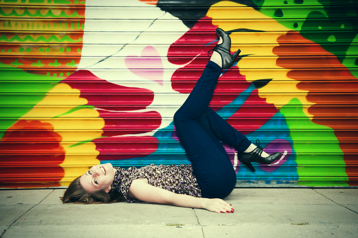 Olivia Pelton lying on the ground in front of graffiti