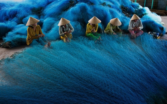 Women in conical hats mending blue fishing nets in Vietnam