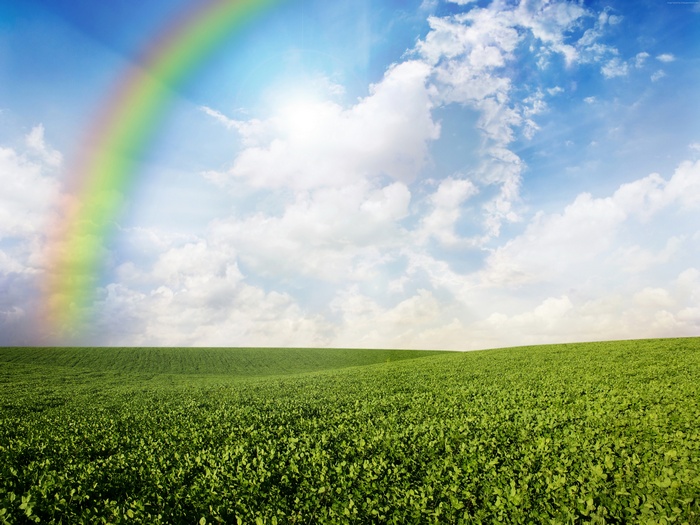 Rainbow over green meadows under a cloudy sky