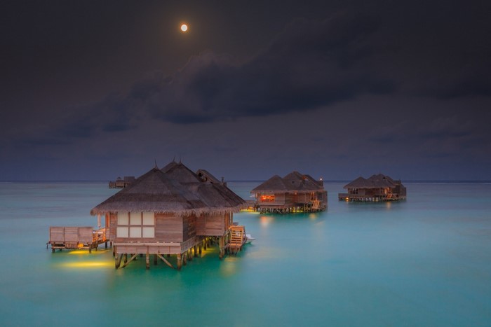 Overwater bungalows at night under the moon in the Maldives