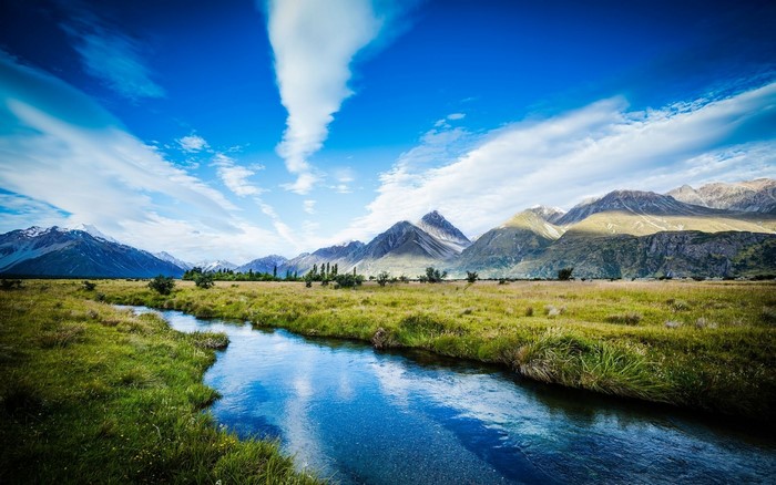 River flowing through a meadow towards mountains under a blue sky