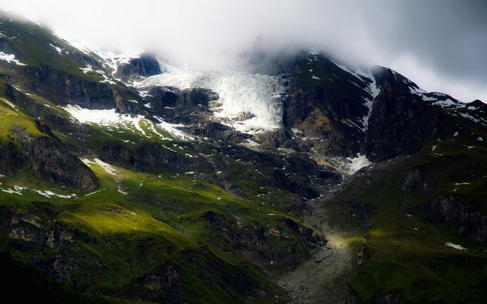 Glacier on a green mountain slope under clouds