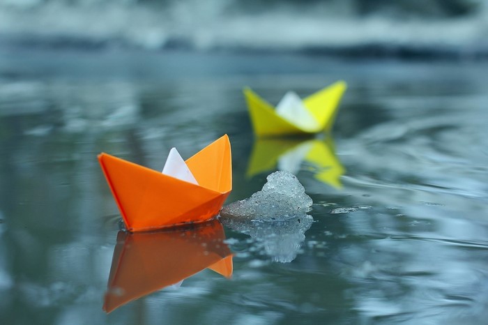 Orange and yellow paper boats floating on water with ice