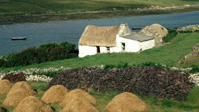 Thatched roof cottage by the water with hay bales
