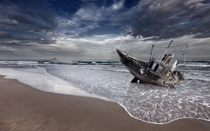 Shipwrecked boat on a sandy beach with stormy clouds