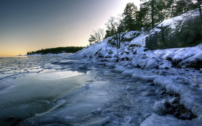 Frozen lake shore with snow-covered rocks and trees