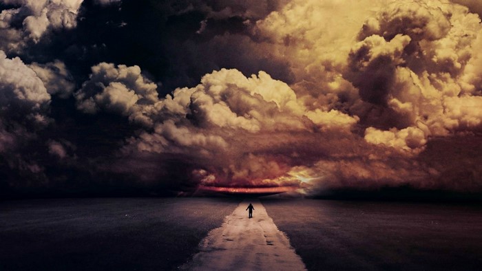 Person walking on a road towards a stormy sky