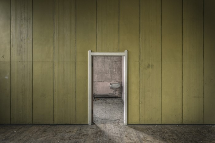 Abandoned room with yellow wood paneling and doorway to sink