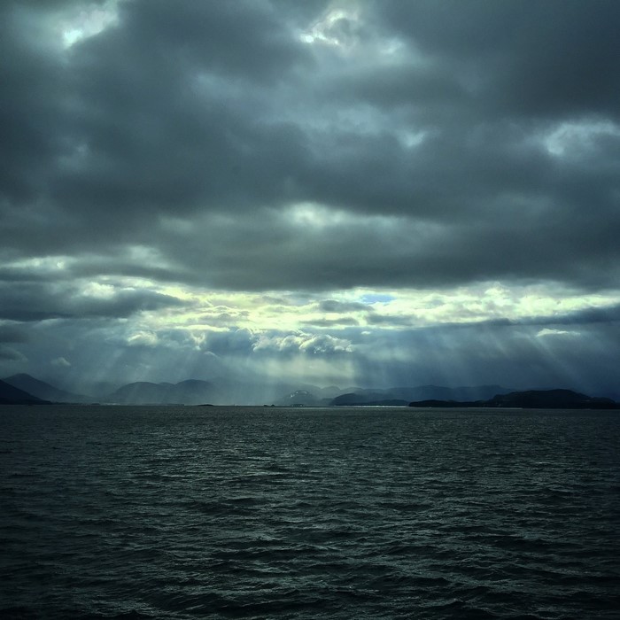 Sun rays breaking through storm clouds over the sea and mountains