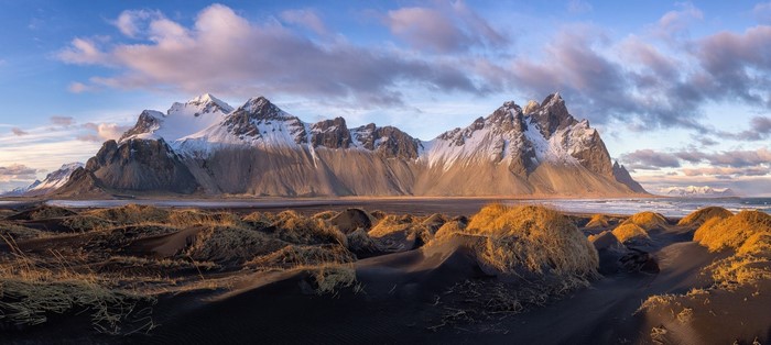 Snow-capped mountains and black sand dunes at sunrise