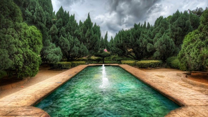 Rectangular pool with fountain in a garden with cypress trees