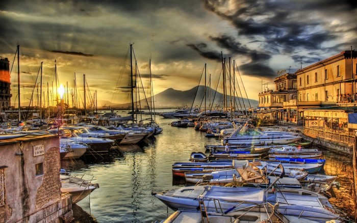 Boats docked in a harbor at sunset with a mountain in the background