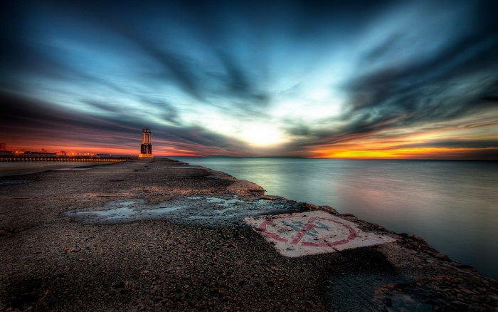 Sunset over the ocean with a lighthouse on a pier