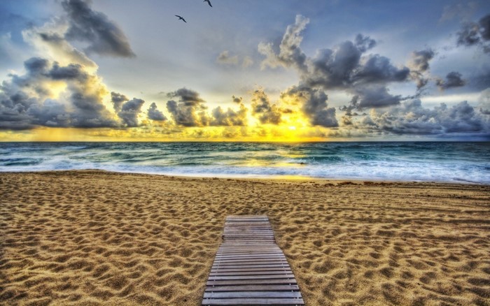 Beach boardwalk at sunrise with ocean waves and clouds