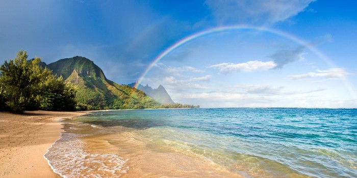 Rainbow over a tropical beach with mountains and ocean