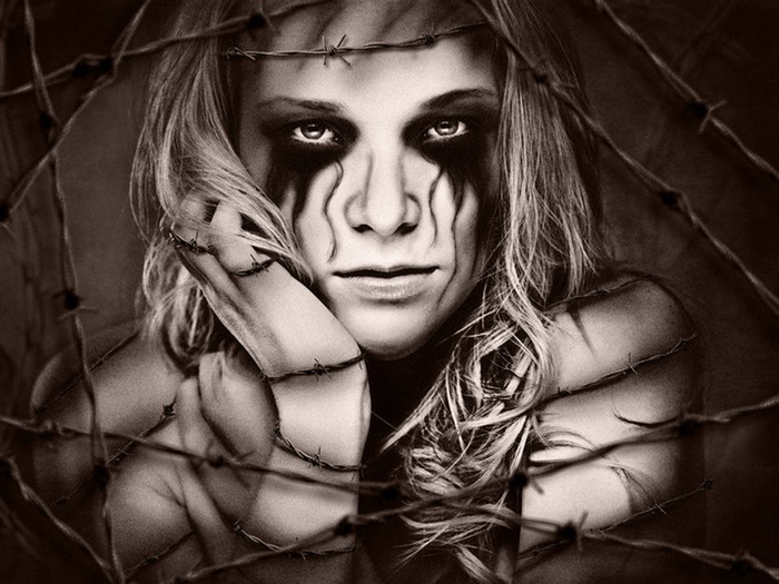 Woman with dark makeup behind barbed wire