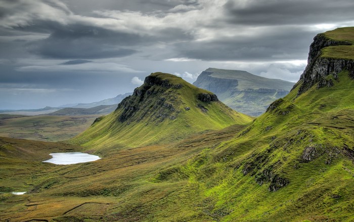Green rolling hills and a small lake under a cloudy sky