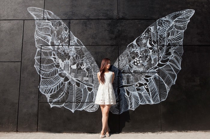 Woman in white dress posing against angel wing mural
