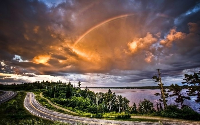 Rainbow over a lake at sunset with a winding road