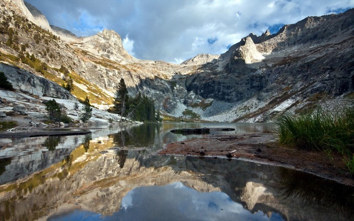 Mountain lake reflecting rocky peaks and cloudy sky