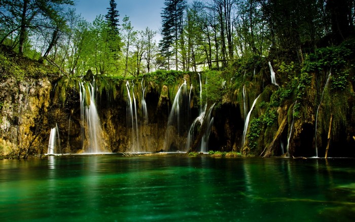 Waterfalls cascading into a vibrant green lake in a forest