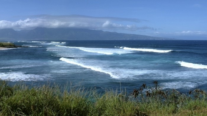 Ocean waves crashing near a mountainous coastline under a cloudy sky