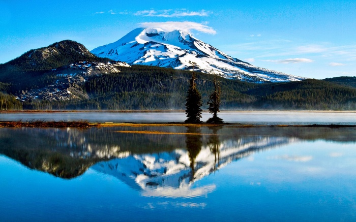 Snow-capped mountain reflected in a calm lake with trees