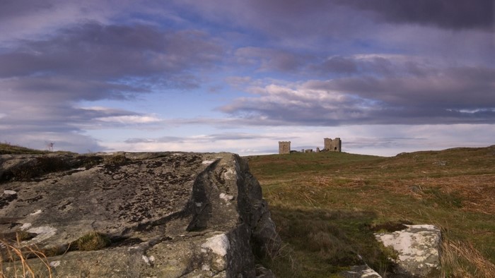 Ruined castle on a grassy hill under cloudy sky
