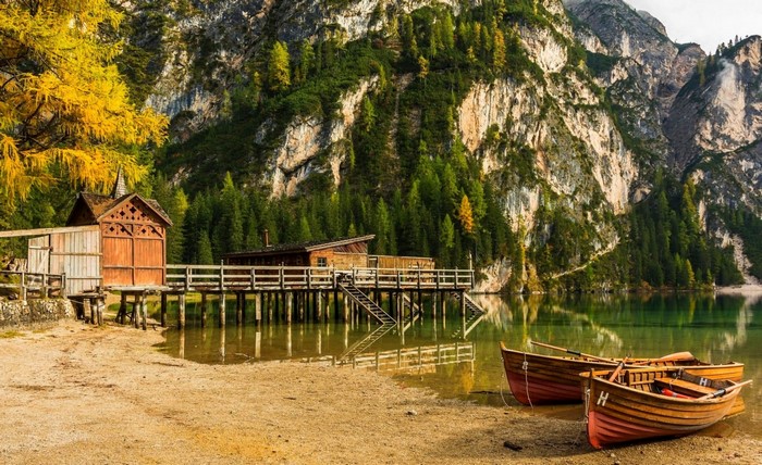 Wooden boats on a sandy beach by a lake with mountains
