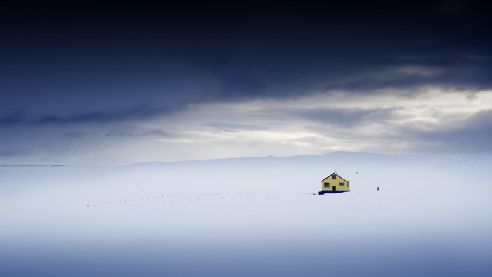 Yellow house in a vast snowy landscape under a dark sky