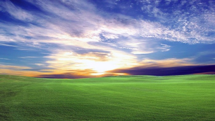 Green rolling hills under a dramatic sunset sky