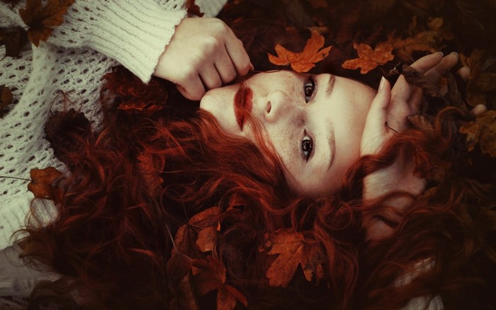 Redhead woman with freckles lying in autumn leaves