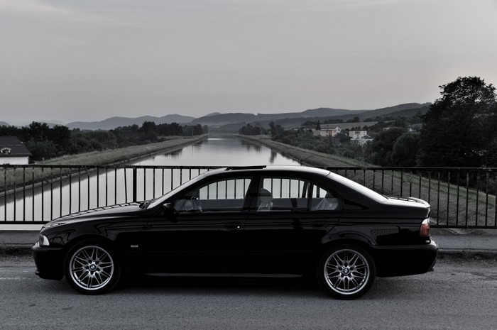 Black BMW 5 Series Sedan parked by a canal
