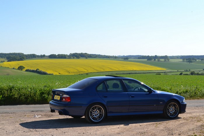 Blue BMW E39 Sedan parked on a dirt road with a yellow field