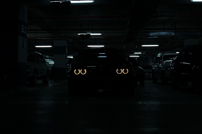 Black BMW E39 with glowing angel eye headlights in a dark parking garage