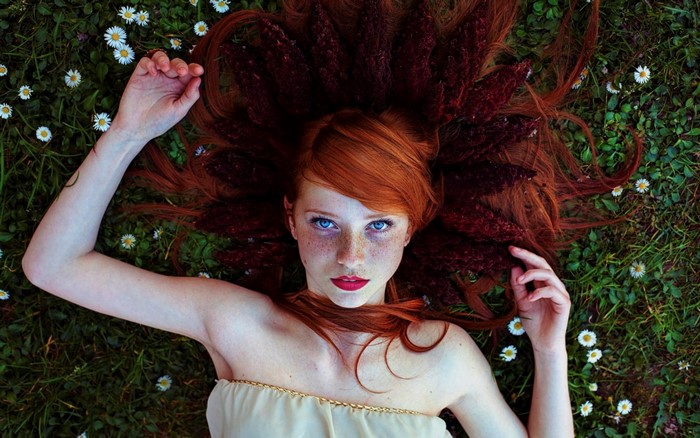 Redhead woman with flowers in hair lying in grass