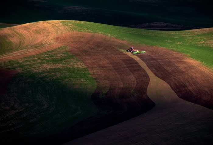 Tractor plowing rolling hills at dusk
