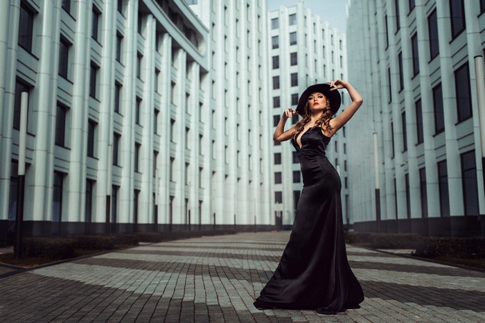Woman in black dress and hat posing in front of modern buildings