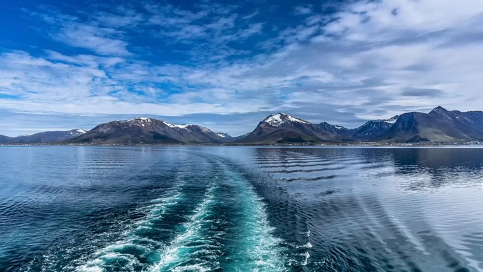 Wake from a boat in front of snow-capped mountains and a blue sky