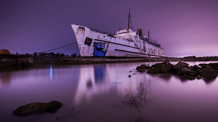Abandoned ship with graffiti on water at dusk