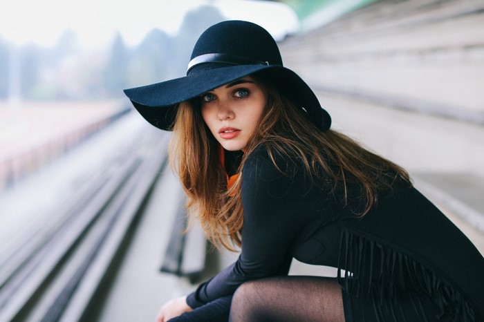 Woman in black hat and dress sitting on bleachers