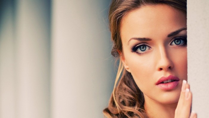 Woman with blue eyes and brown hair peeking from behind a wall